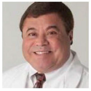 A man in a white coat and tie is smiling for the camera.